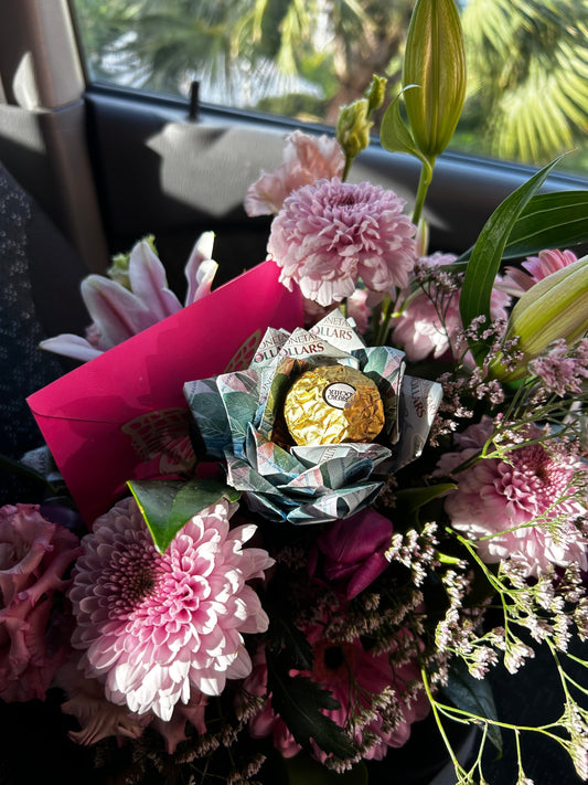 A fresh flower arrangement with money roses, chocolate, and a card